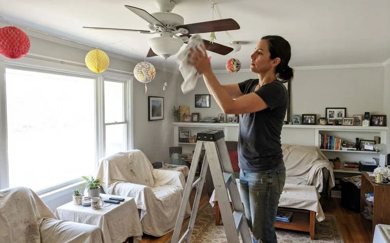 A family member standing on a stool to dust ceiling fan blades ahead of festive spring cleaning at home